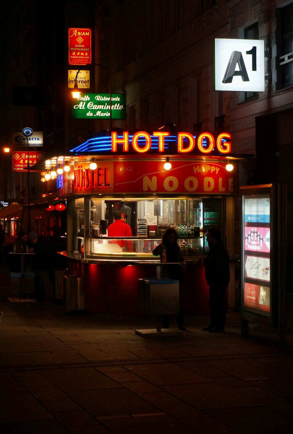 people walking on sidewalk near red and white store during nighttime