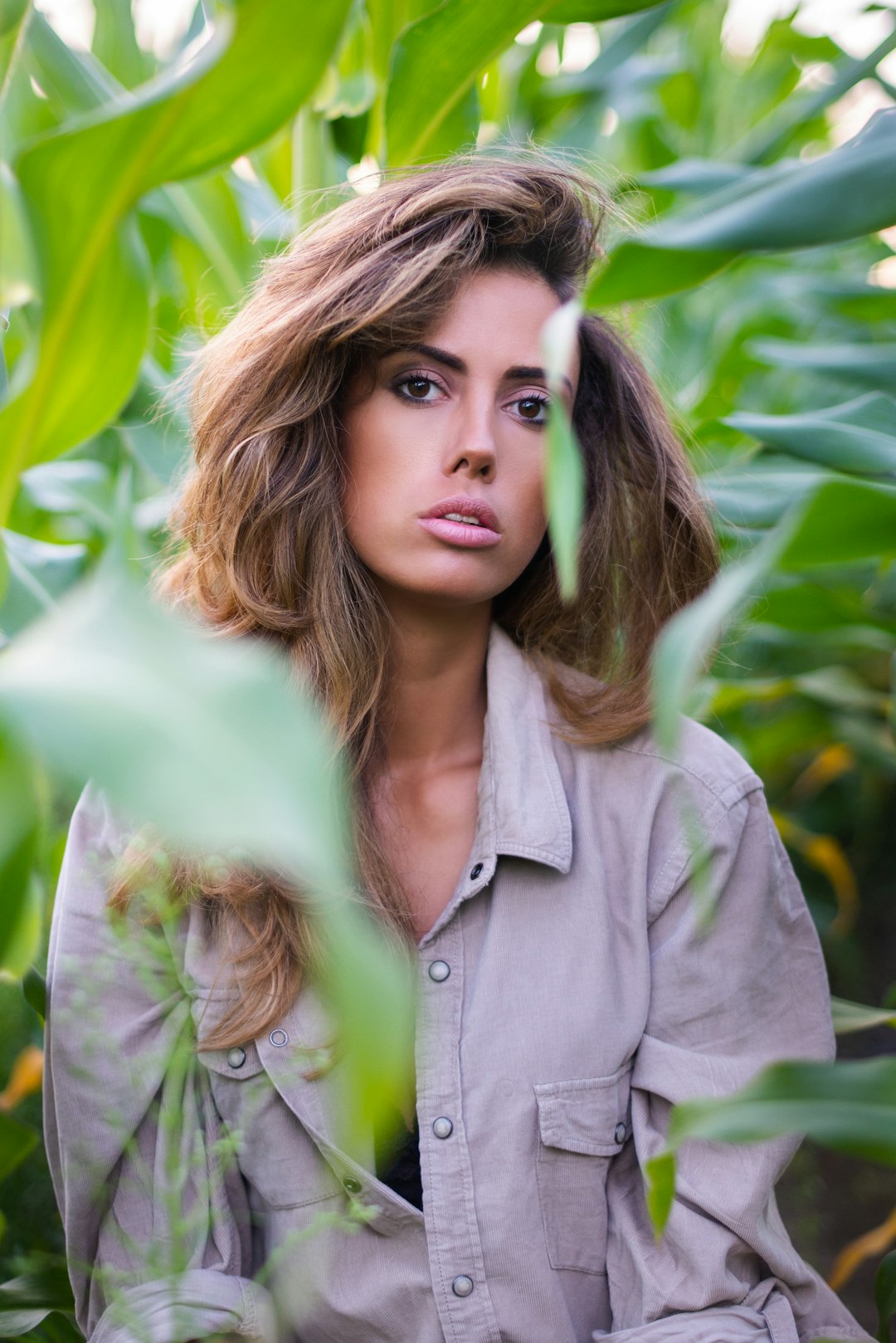 woman in gray button up shirt standing near green leaves