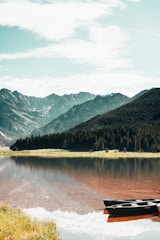 lake near green trees and mountain under blue sky during daytime