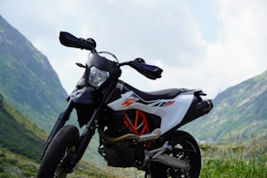 Side profile of a bright orange adventure bike parked on a rugged mountain trail.