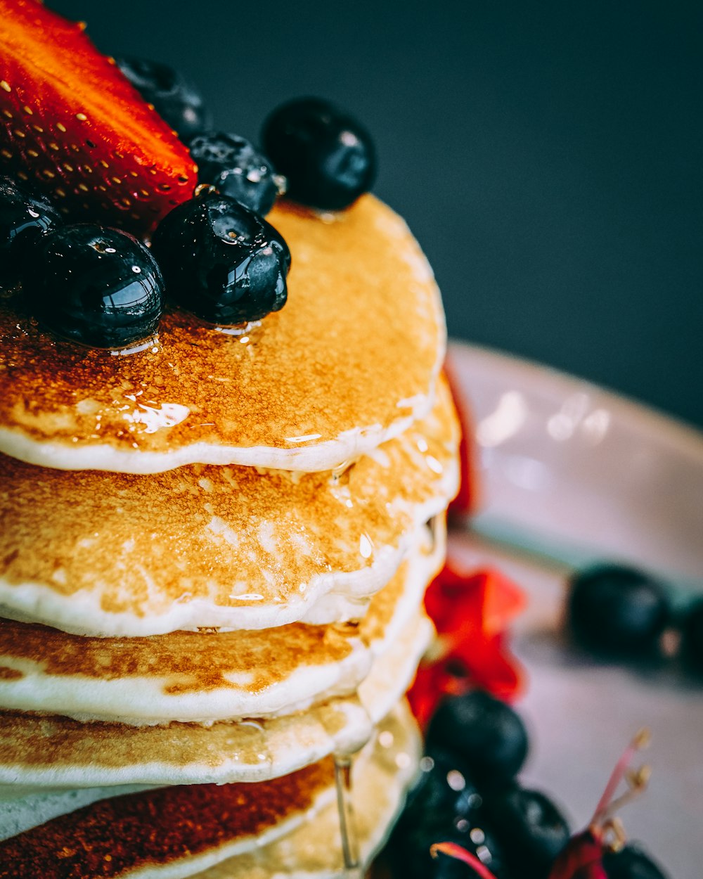 Pancake con fragole a fette e bacche nere su piatto di ceramica bianca