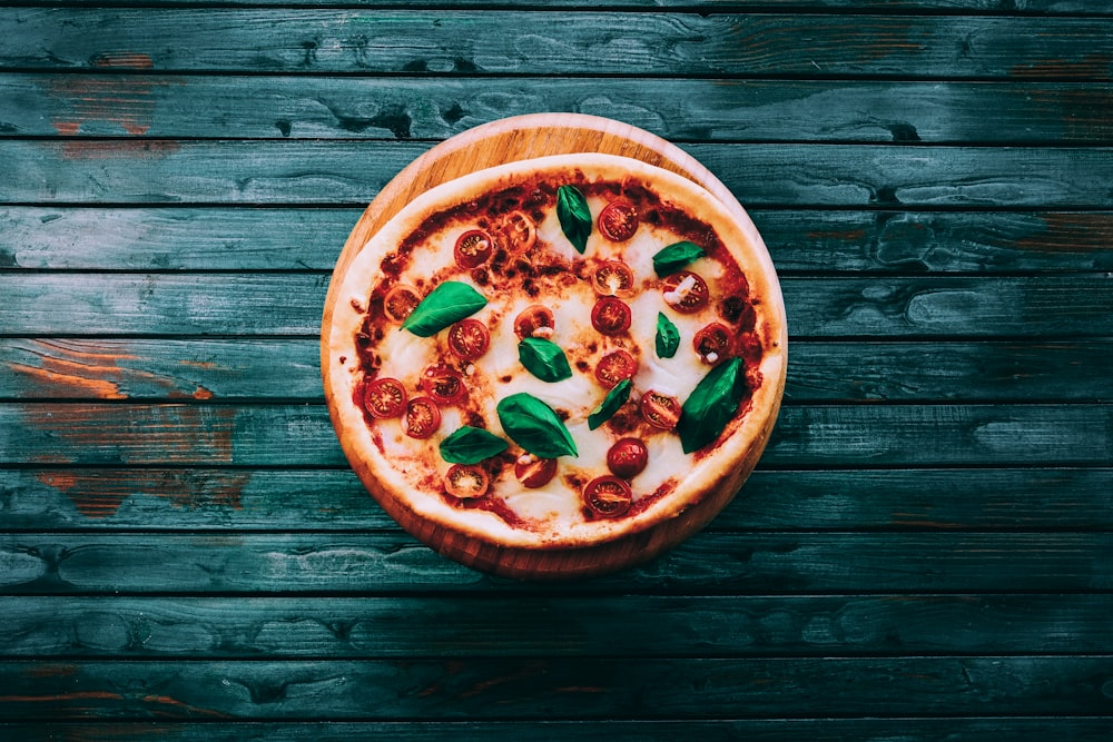 pizza with red and green leaves on brown wooden table