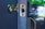 A close-up view of a door with a brass doorknob and a latch plate. The latch plate is engraved with the brand name Kwikset. The background is softly blurred with hints of greenery and light, suggesting an outdoor setting.