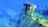 A submerged shipwreck rests on the ocean floor, surrounded by deep blue water. The ship's hull is partially intact, with visible metal structures and scattered debris. The scene evokes a sense of stillness and mystery beneath the sea.