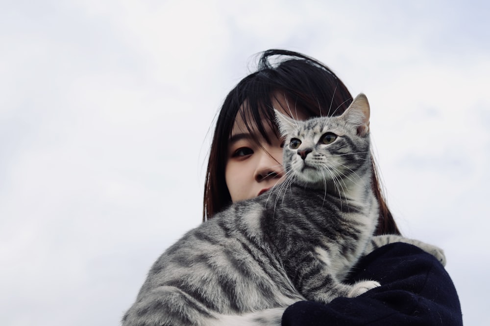 woman in black jacket holding silver tabby cat