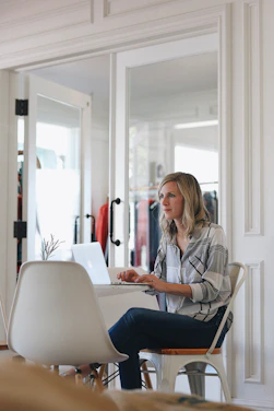 A focused professional woman working remotely on a laptop with organized paperwork around her.