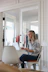 A smiling woman working on a laptop in a bright, minimalist home office.