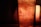 A close-up of a glass filled with a fizzy beverage featuring ice cubes and bubbles. The lighting creates a warm, amber glow, and the glass bears a logo. The ambiance is cozy and dimly lit.