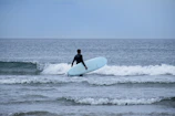 An instructor helping a beginner adjust their wetsuit before heading into the waves.