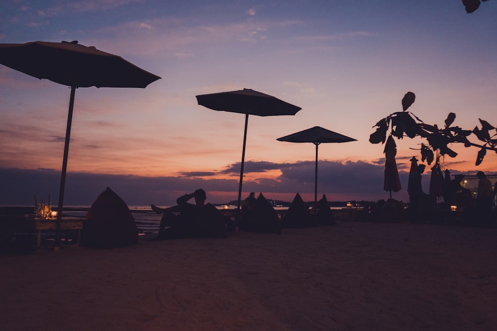 silhouette of people sitting on beach chairs under umbrella during sunset