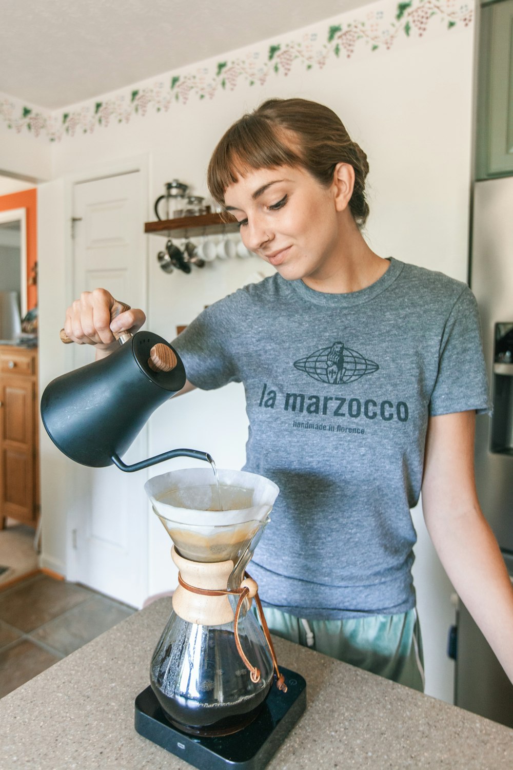 woman in gray crew neck t-shirt pouring black ceramic mug to clear glass cup