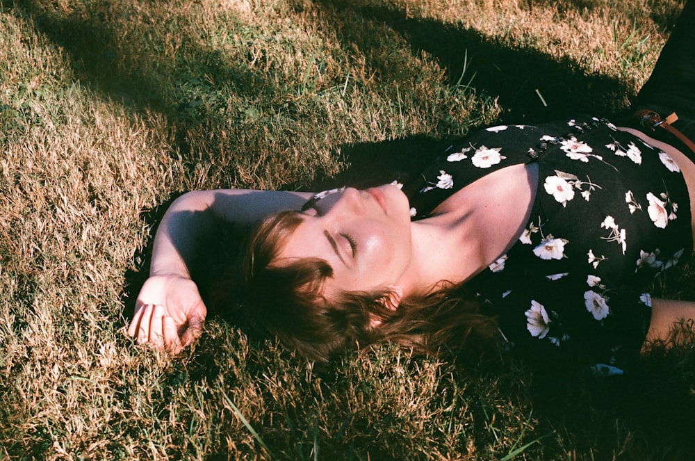 woman in black and white floral dress lying on green grass field