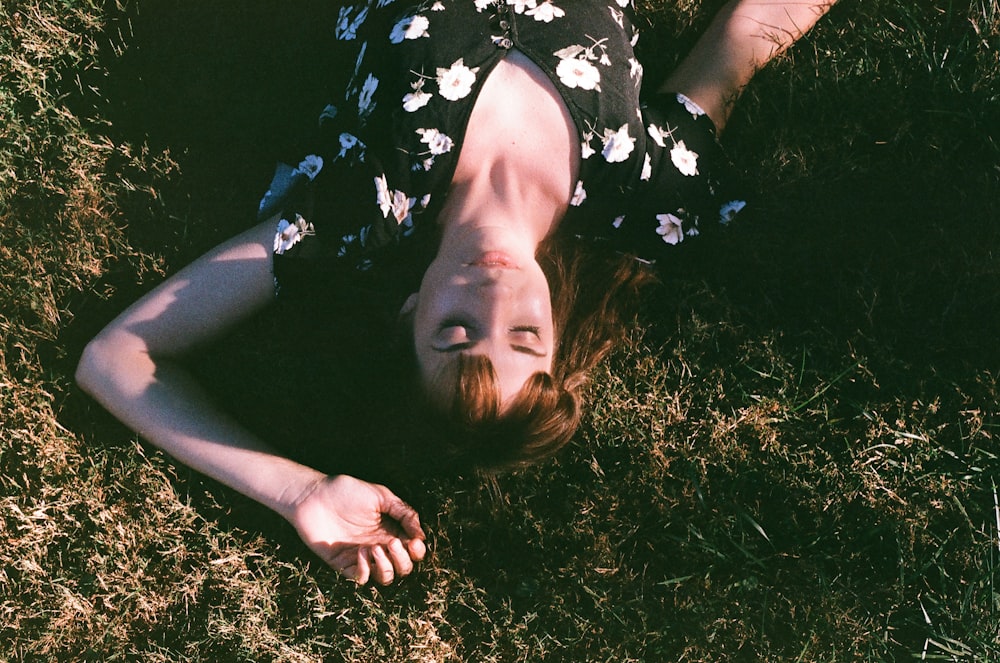 woman in black and white floral dress lying on green grass field