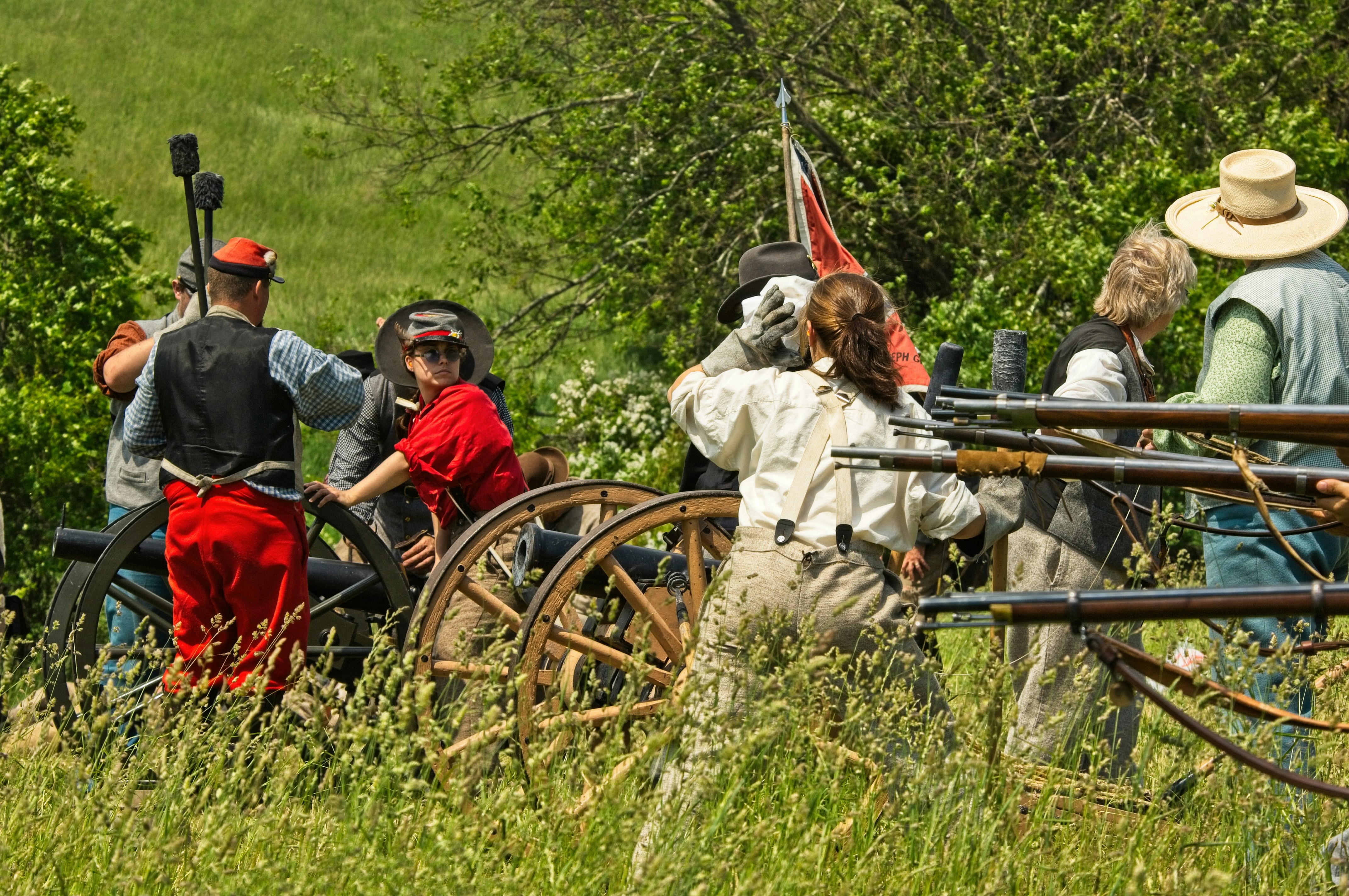man in gray coat and red hat riding red and black wooden carriage, Reenactment of a civil war battle.