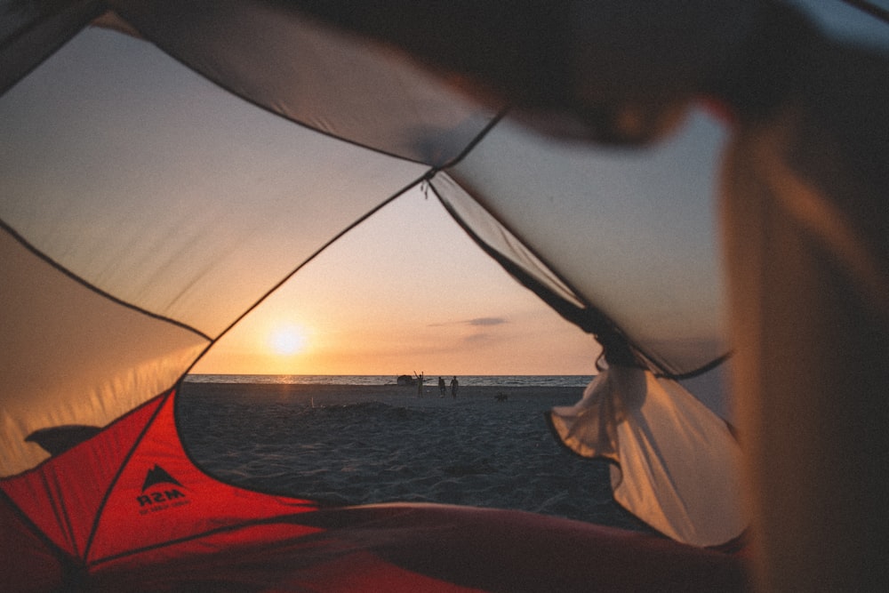 person in white shirt holding white and red umbrella near body of water during sunset