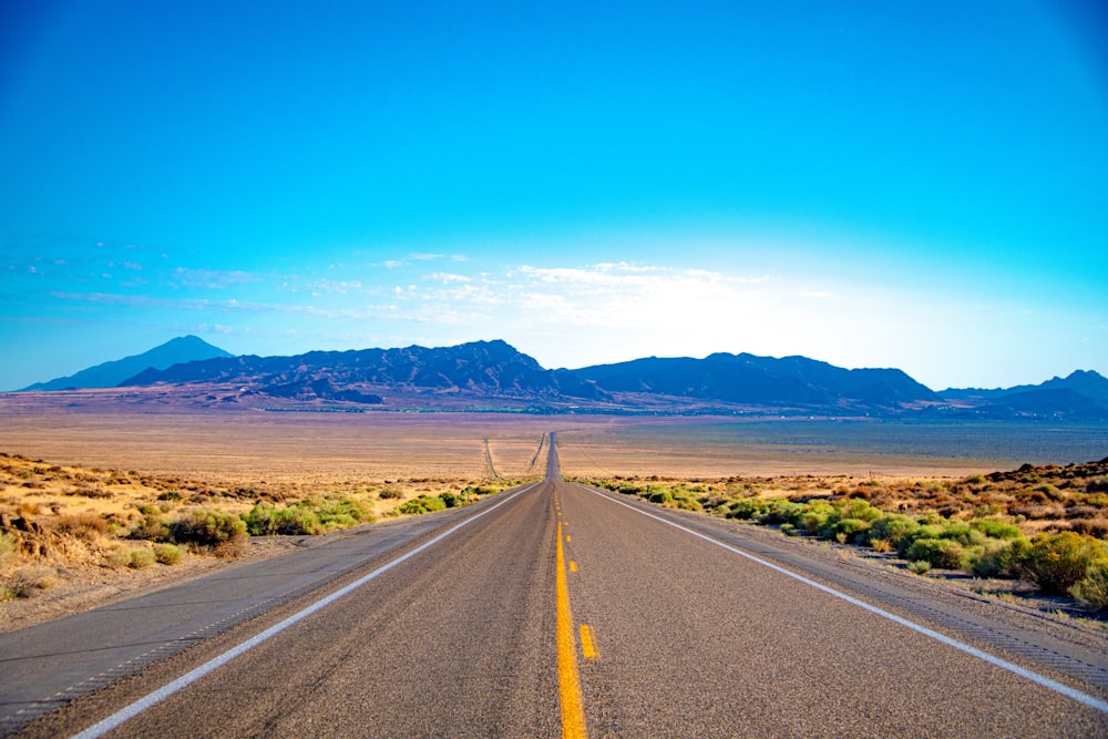 gray concrete road near green grass field under blue sky during daytime