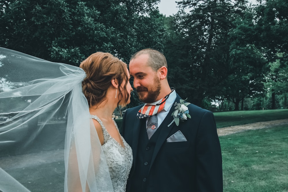 uomo in abito nero che bacia la donna in abito da sposa bianco