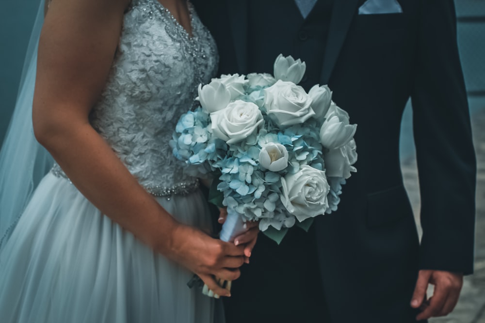 mulher no vestido de noiva floral branco que segura o buquê de rosas brancas