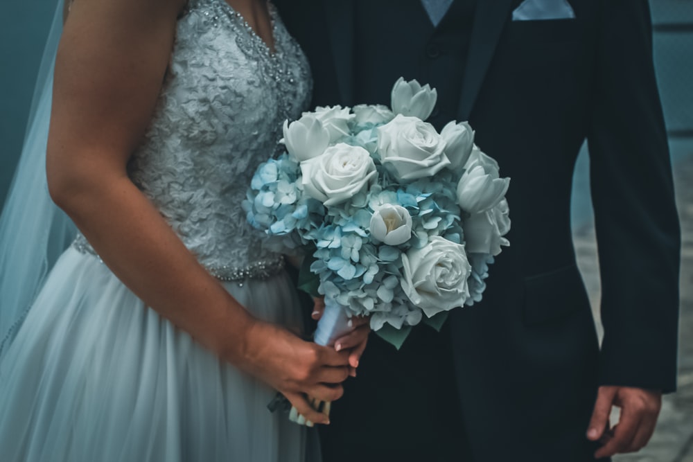 Frau in weißem geblümtem Brautkleid mit einem Strauß weißer Rosen