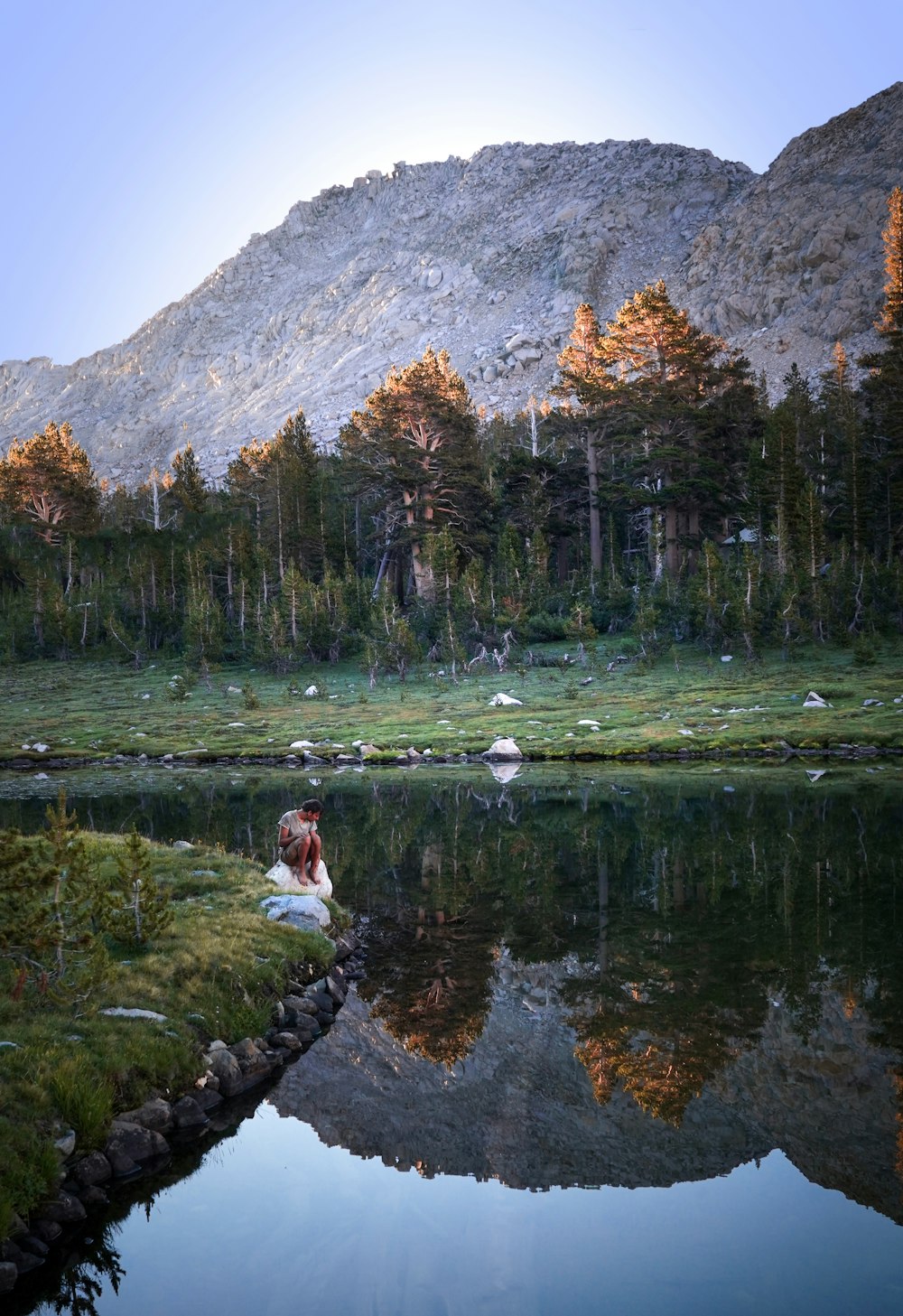 person sitting on rock near lake during daytime