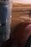 The image displays a close-up of a section of a large vehicle, likely a truck. A polished metallic exhaust pipe features prominently on the left, with a brown fender showing decorative details on the right. The vehicle's surface is smooth and reflective, with an emblem visible.