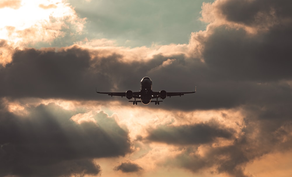 silhouette of airplane under cloudy sky during daytime