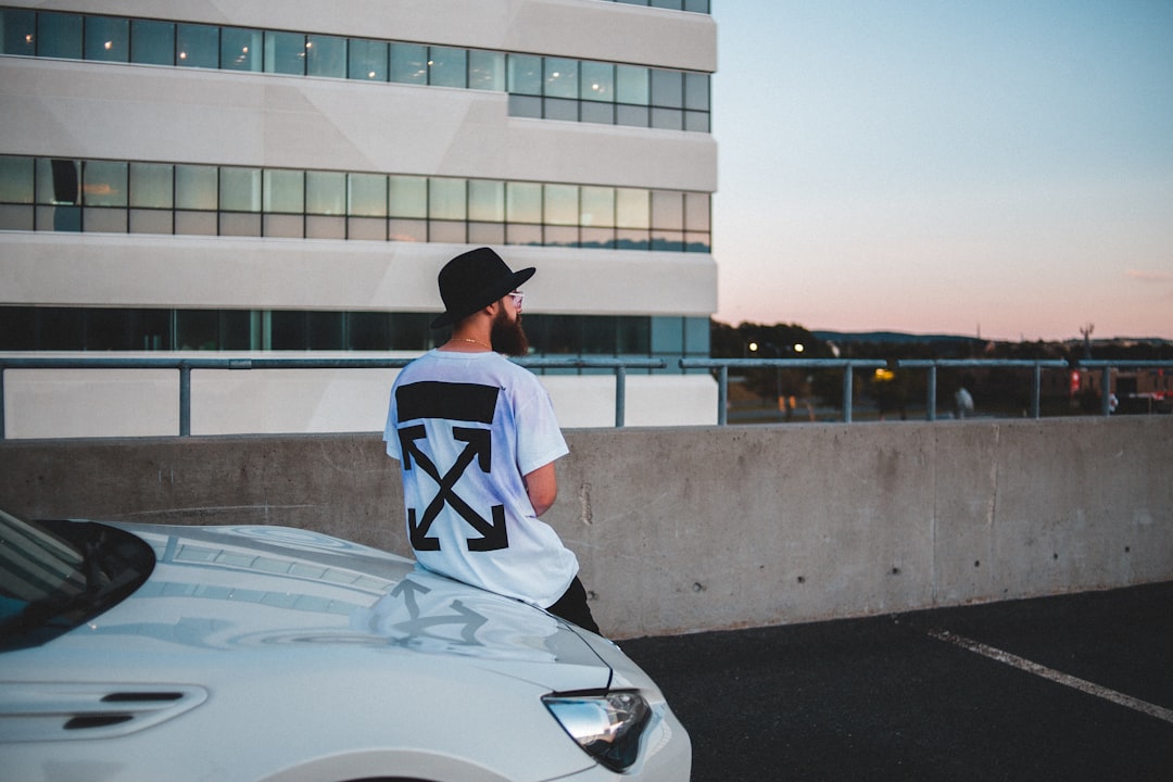 man in white and black jersey shirt and black cap sitting on white car