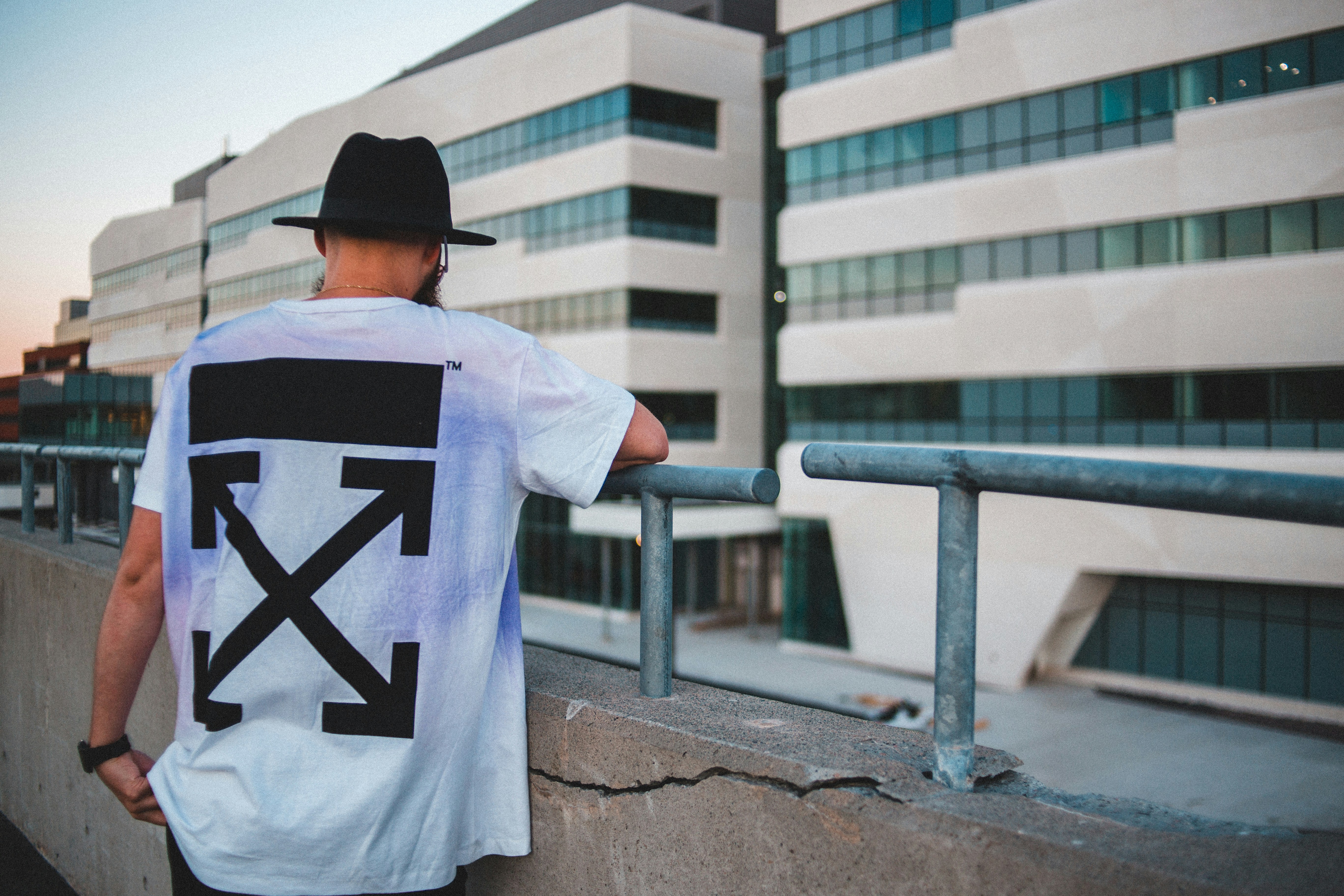 man in white and black t-shirt and black cap standing near blue metal railings during