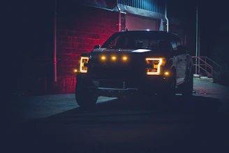 Bright headlights glowing on a sleek pickup truck at dusk.