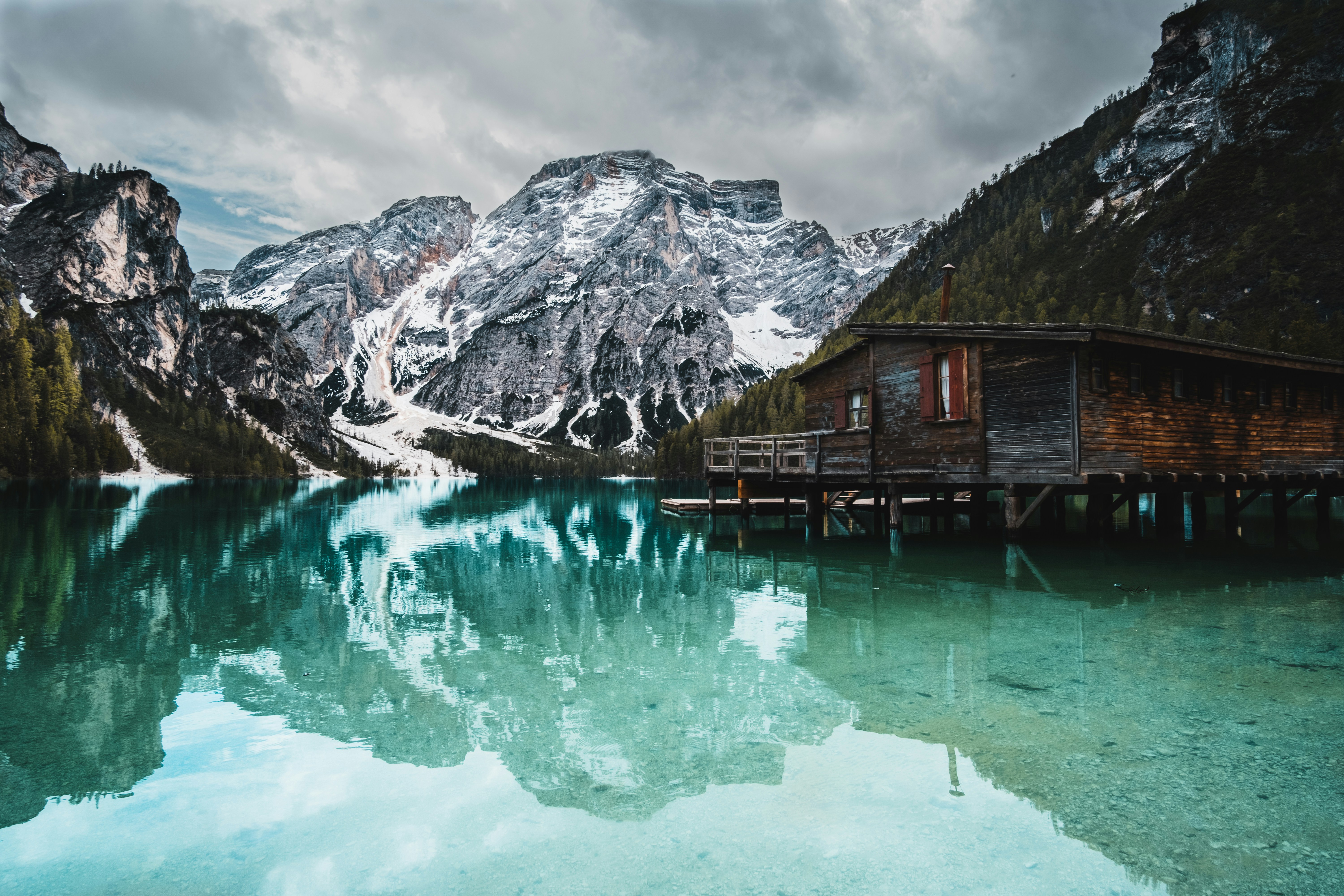 Casa di legno marrone sul lago vicino alla montagna innevata durante il giorno