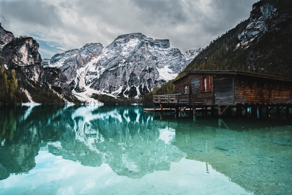 casa de madeira marrom no lago perto da montanha coberta de neve durante o dia