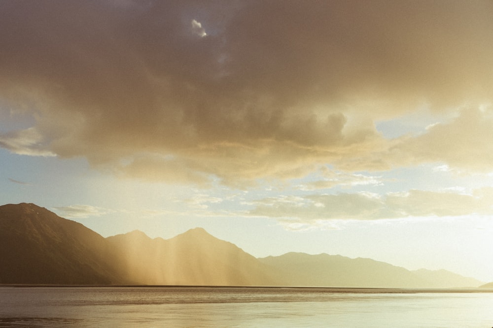 body of water near mountain under cloudy sky during daytime