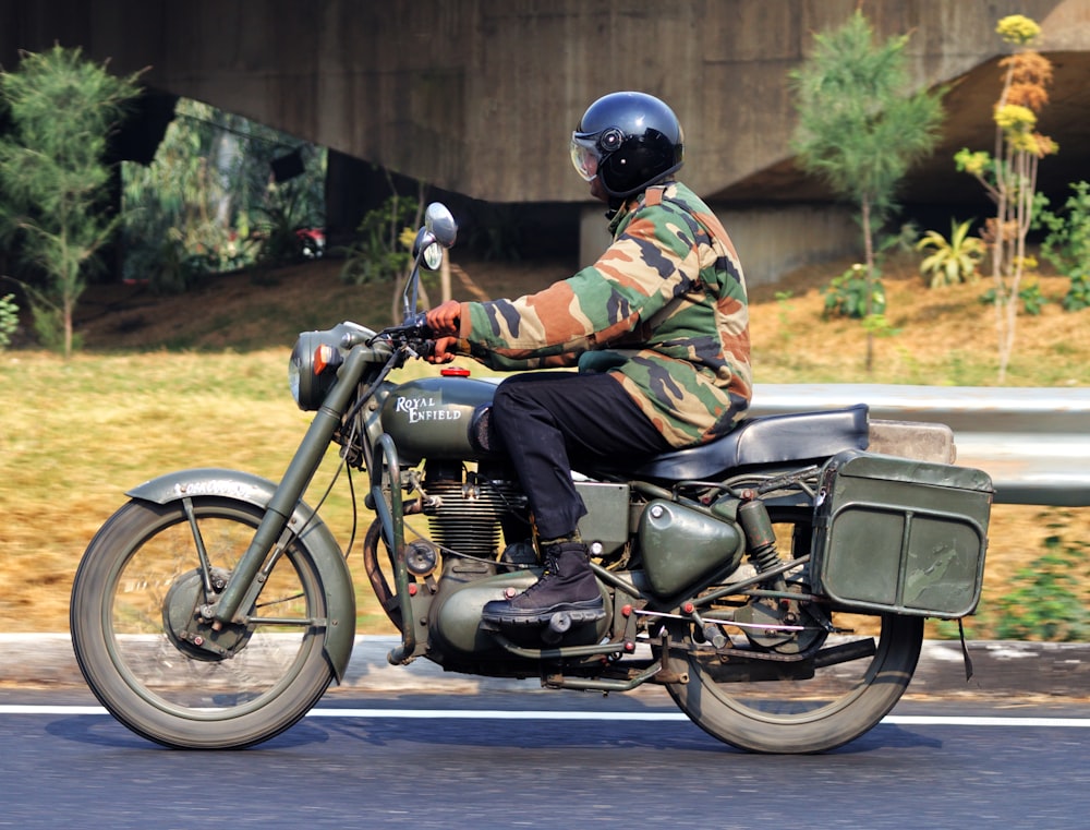 man in green brown and black camouflage jacket riding on black motorcycle during daytime