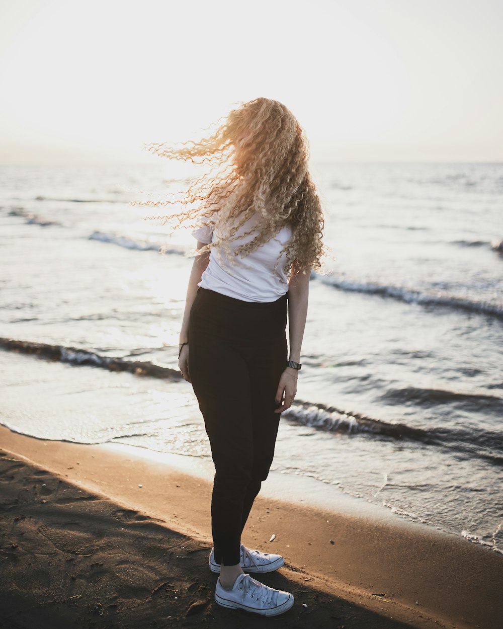 woman in white shirt and black pants standing on beach shore during daytime