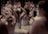 A group of young ballet dancers practice their routines, wearing white tutus and leotards. They are positioned closely together, with their arms raised gracefully in various ballet poses. The background is blurred, focusing attention on the intricate movements of the dancers.