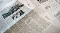 A collection of printed newspapers with articles containing texts, images, and graphs spread out. The layout includes columns of text, black and white photographs, and statistical graphs, conveying information on a flat surface.