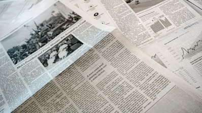 A collection of printed newspapers with articles containing texts, images, and graphs spread out. The layout includes columns of text, black and white photographs, and statistical graphs, conveying information on a flat surface.
