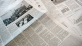 A collection of printed newspapers with articles containing texts, images, and graphs spread out. The layout includes columns of text, black and white photographs, and statistical graphs, conveying information on a flat surface.