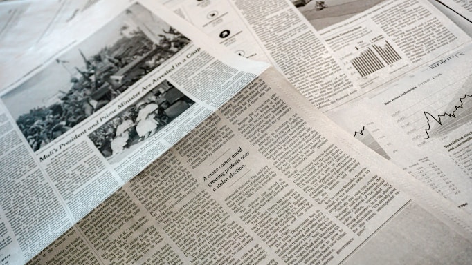 A collection of printed newspapers with articles containing texts, images, and graphs spread out. The layout includes columns of text, black and white photographs, and statistical graphs, conveying information on a flat surface.