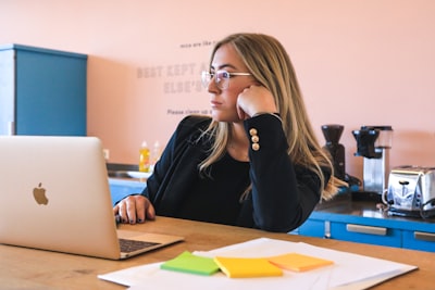 woman in black long sleeve shirt wearing black framed eyeglasses using macbook bored teams background