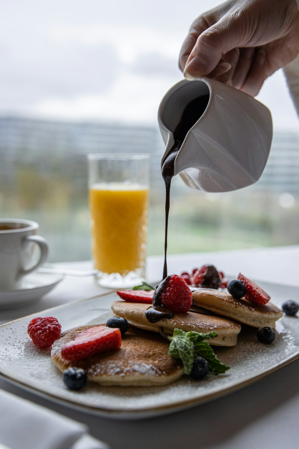 a person pouring syrup on a plate of pancakes