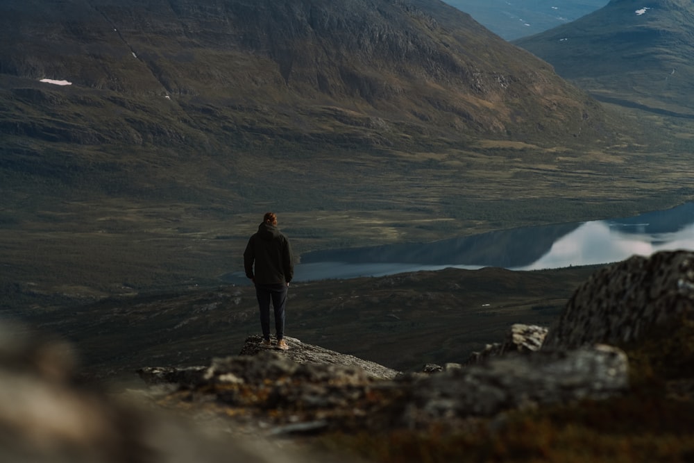 man in black jacket standing on rock formation near body of water during daytime