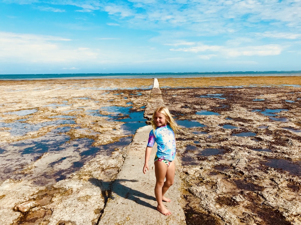 menina no biquíni azul e branco em pé na costa rochosa durante o dia