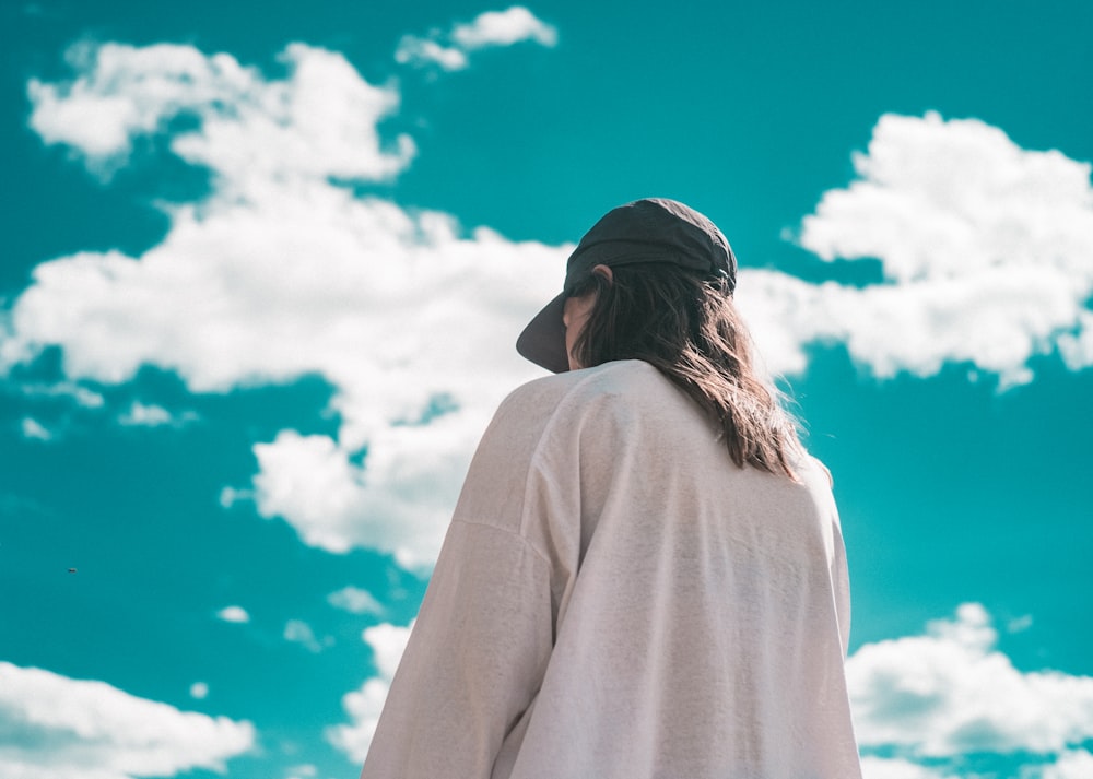 woman in white long sleeve shirt and black cap under white clouds and blue sky during