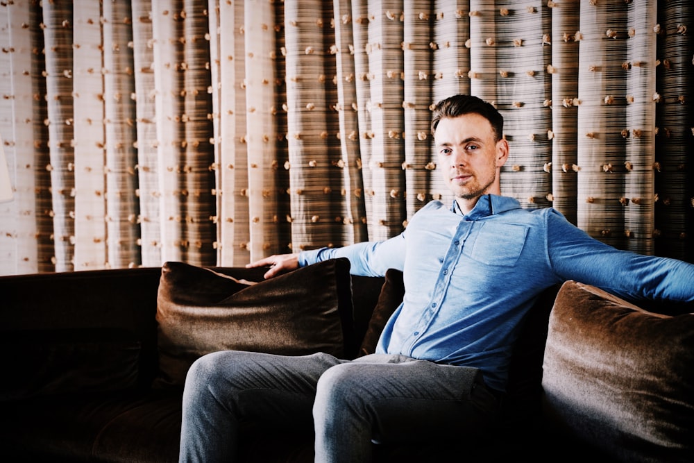 man in blue denim jacket sitting on brown sofa chair