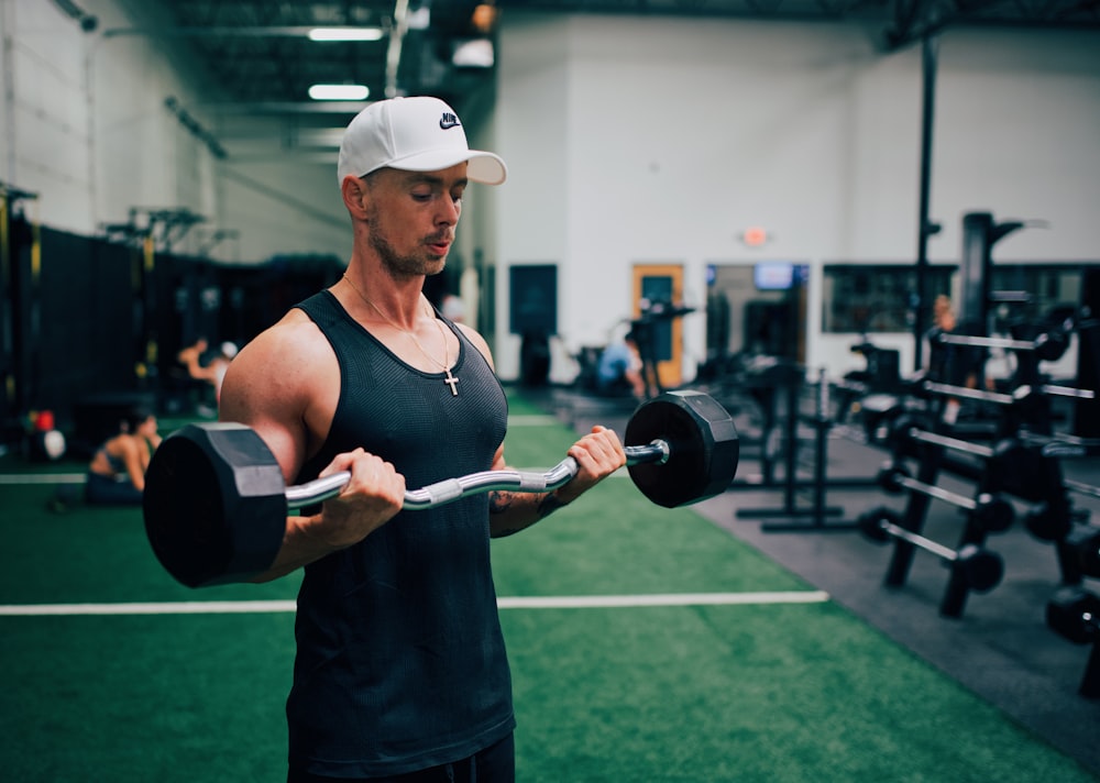 man in black tank top and white cap holding black and gray dumbbell