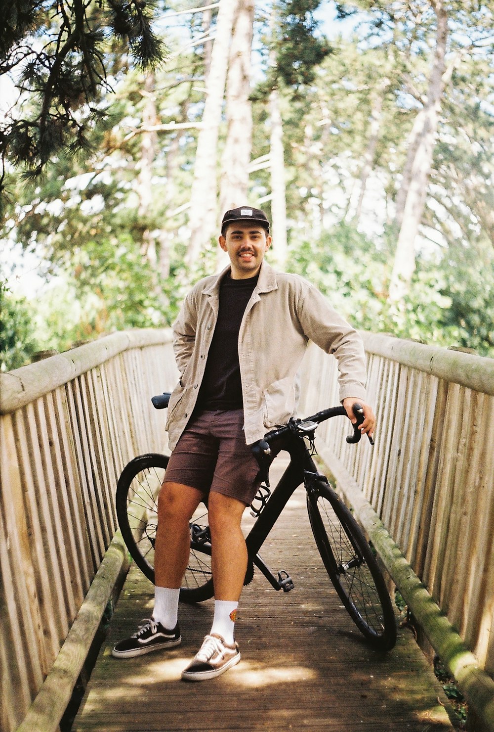 Hombre con chaqueta marrón y pantalones cortos negros montando bicicleta negra