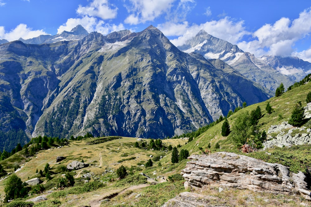 green grass field near mountain under blue sky during daytime