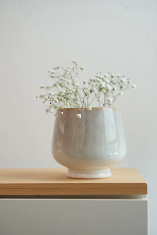 Close-up of a modern white ceramic vase holding fresh flowers on a clean, uncluttered shelf.