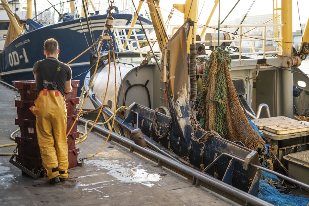 homem na jaqueta amarela de pé ao lado do barco branco durante o dia